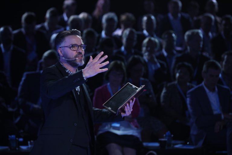 Antoni Lacinai agerar moderator med publik i bakgrunden